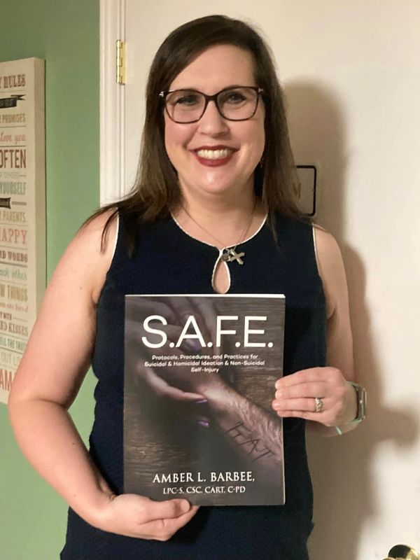 Woman holding a book titled S.A.F.E. by Amber L. Barbee.