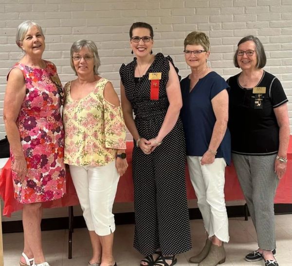 Five women standing together indoors, smiling for a group photo.
