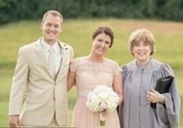 A happy couple and an officiant posing outdoors at a wedding.
