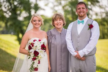 Newlywed couple posing with officiant outdoors on a sunny day.