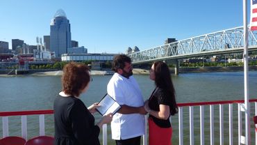 Couple exchanging vows by the river with an officiant nearby.