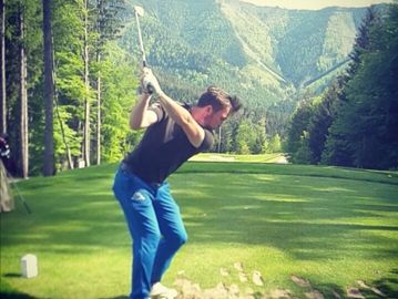 Man in blue pants preparing to swing a golf club on a lush course.