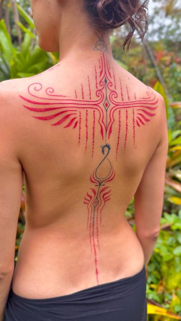 Intricate red and black tribal tattoo covering a woman's upper back and spine.