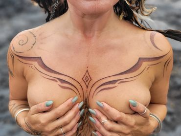 Intricate symmetrical chest and shoulder tattoos on a person with painted nails.