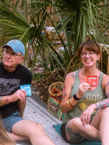Two people sitting outdoors holding colorful packets, surrounded by greenery.