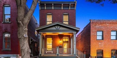 A cozy brick house with a front porch lit warmly at dusk.