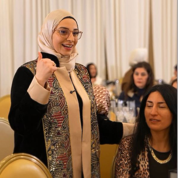 A woman in a patterned hijab and glasses gestures positively at a seated woman in a leopard print top.