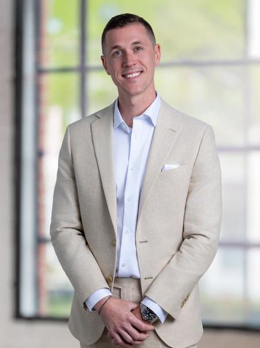Man in light beige suit smiling indoors.