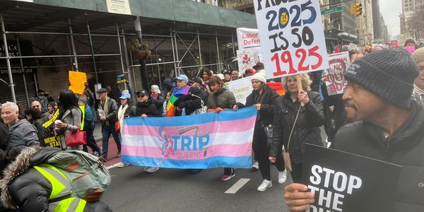 A diverse group marches with banners advocating LGBTQ+ rights and social justice.