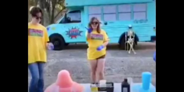 People in yellow shirts playing a game near a blue bus and skeleton.