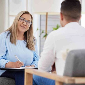 A woman listens attentively while taking notes during a conversation.