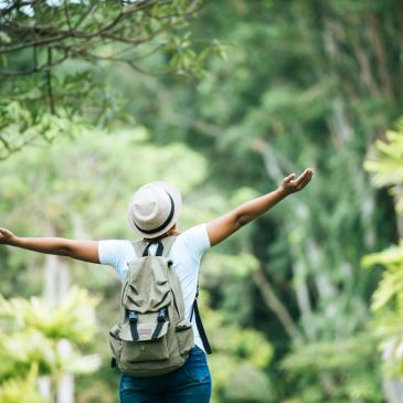 Person with backpack and hat enjoying nature with arms wide open.