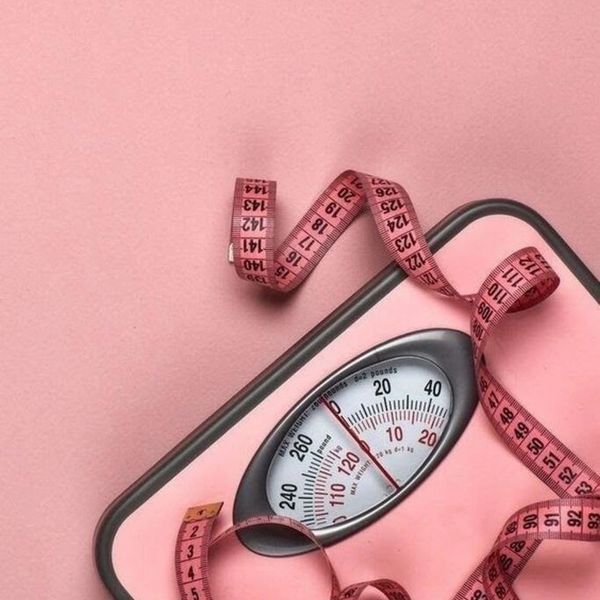 Pink weighing scale with a pink measuring tape on a pink background.