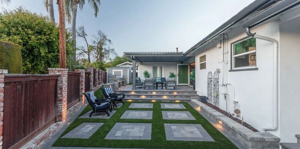 Modern backyard with patio seating and stepping stones on artificial grass.
