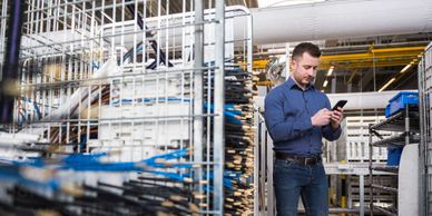 Man using smartphone in an industrial warehouse filled with metal racks.