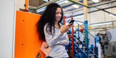 A woman with curly hair checking her phone in an industrial setting.