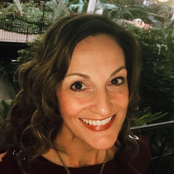 A close-up portrait of a smiling woman with curly hair.