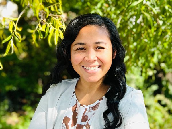 Smiling woman outdoors with greenery background.