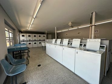 A clean, well-lit laundry room with washers, dryers, and seating.