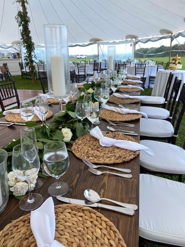 Elegant outdoor dining table set with greenery and candles under a tent.