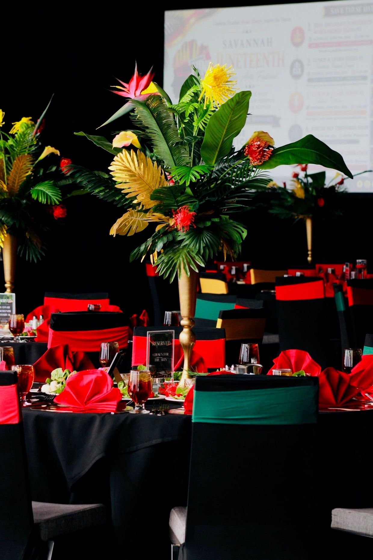 Elegant banquet tables with tropical floral centerpieces and vibrant red, green, and yellow decor.
