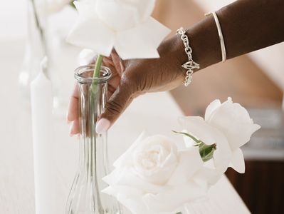 Hand placing white rose in glass vase.