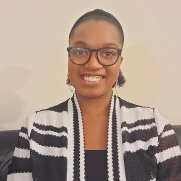 Smiling woman wearing glasses and a black-and-white patterned jacket.