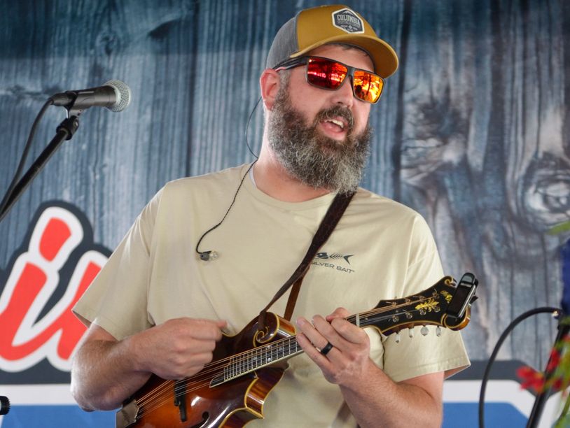 Man playing mandolin on stage with microphone.