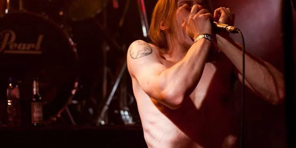 Shirtless male singer passionately performing on stage with microphone in hand.