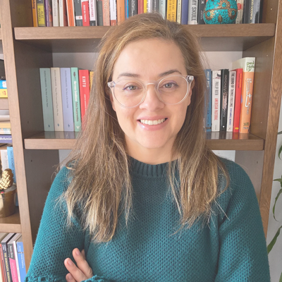 Mujer con gafas cruzando los brazos al frente de una biblioteca