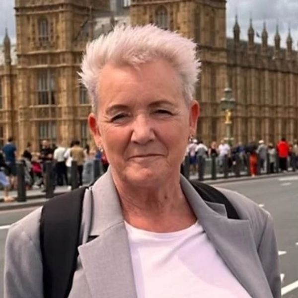 Older woman with short white hair stands confidently near a historic building.
