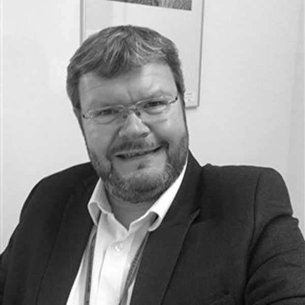 Smiling man in glasses and suit jacket, seated indoors.
