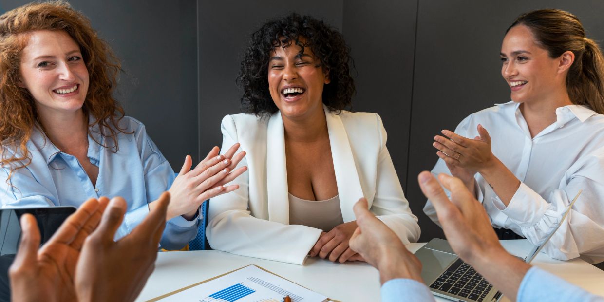 Colleagues applauding a happy woman in a meeting.