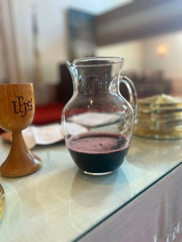 Glass pitcher with red liquid beside a wooden cup.