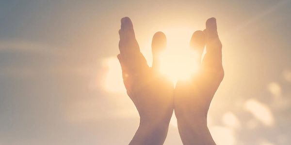 Hands gently cupping the bright sun against a clear sky.