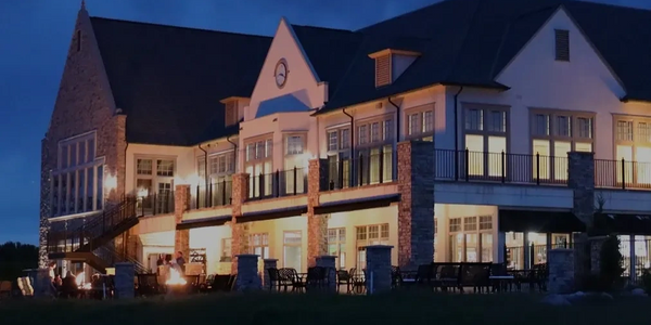 Large illuminated house at night with outdoor seating and fire pits.