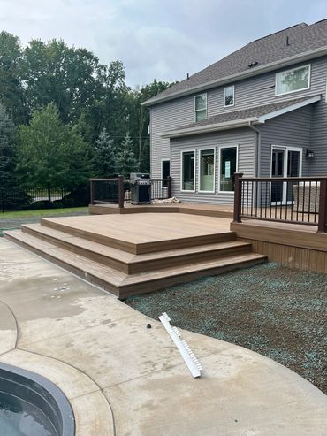 Large wooden deck attached to a modern house with a grill and concrete patio.