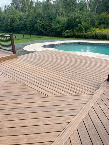 Modern wooden deck surrounding a backyard pool with lush greenery.