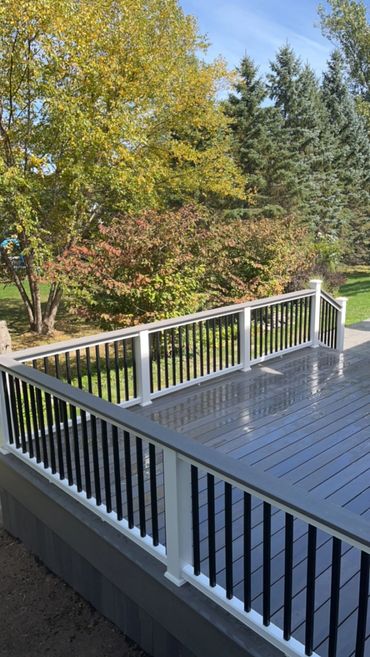 Shiny freshly painted deck with black and white railing surrounded by trees.