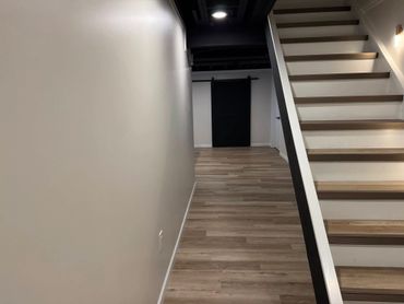 Modern basement hallway with wooden stairs and black sliding door.
