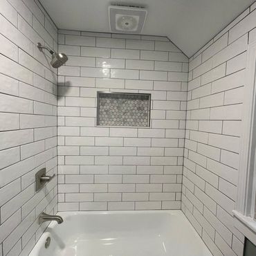 Modern white tiled bathroom with bathtub and shower.