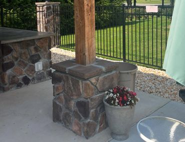 Stone pillar with wooden post next to a flower pot on a patio.