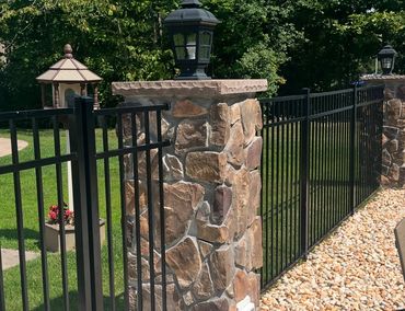 Stone pillars with black metal fencing and lanterns surround a green garden area.