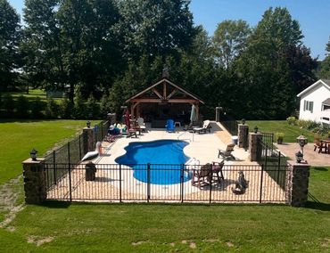 A backyard pool area with chairs, a pavilion, and a fenced enclosure.