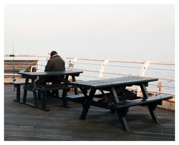 A person sitting alone on a bench at a pier during daytime.