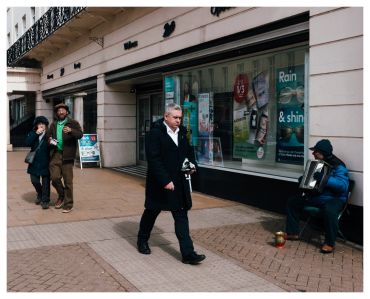 Man walking past street musician playing accordion on sidewalk.