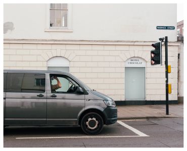 A person in a gray van waits at a red light near a building marked 'Hotel Chocolat'.