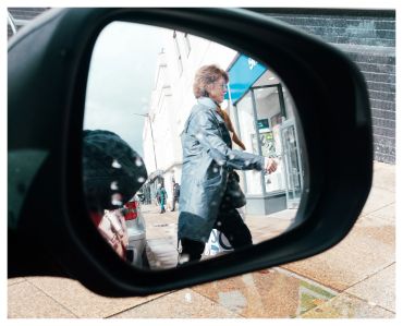 Person walking past a street reflected in a car's side mirror.