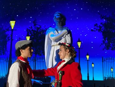 Two people in period costumes pose under a starry sky near a statue.