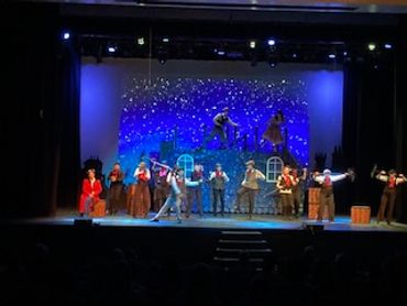 Actors perform a vibrant stage play with a starry backdrop.
